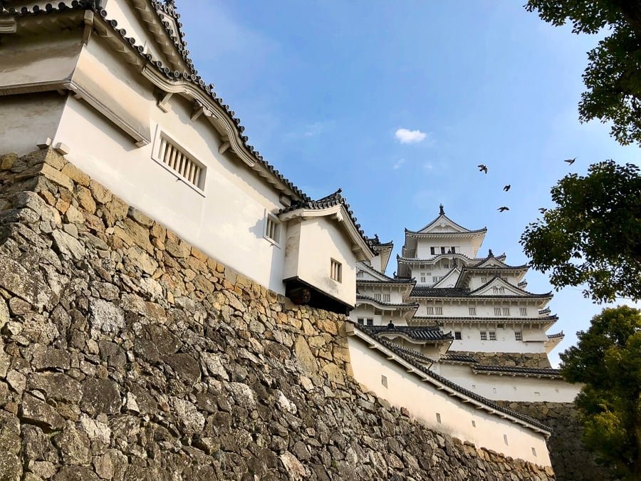 Pájaros volando sobre las empinadas paredes del Castillo Himeji en Japón