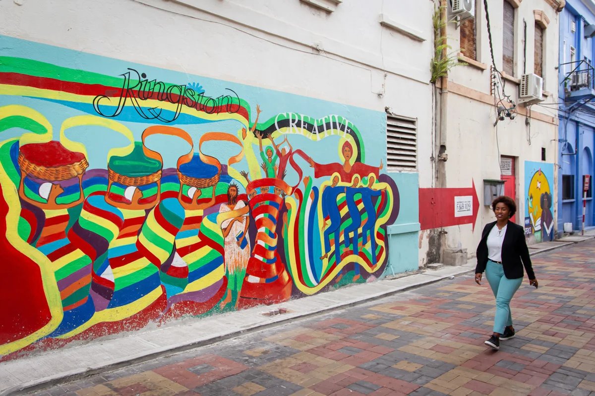 Un mural con muchos colores que dice Kingston y una mujer que pasa junto a él.